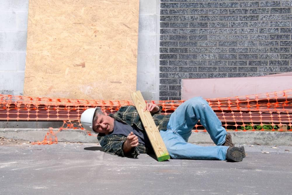 a fallen and injured construction worker in a hard hat laying on the ground at a construction work site