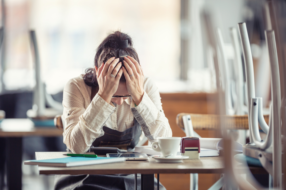 female busines owner holds her head in hands in desperation over paperwork and tax declaration in a closed pub