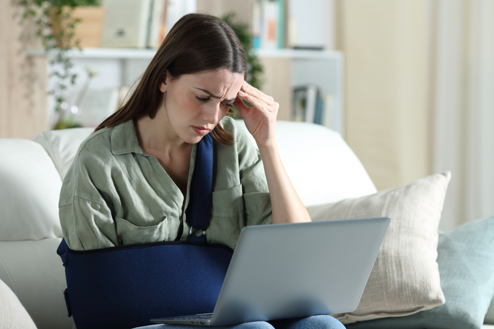 worried handicapped woman reading bad news on laptop sitting on a couch in the living room at home