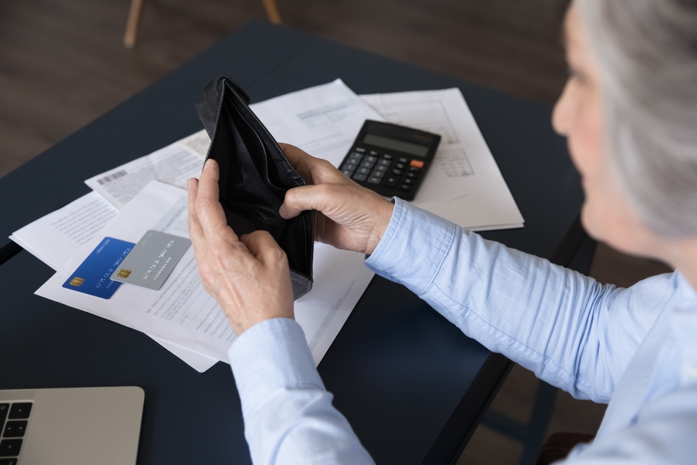 senior woman sit at desk opening empty purse, no banknotes