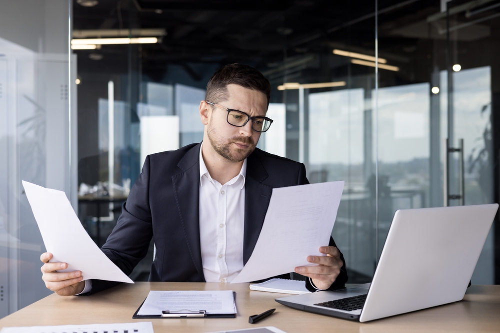 A worried young man businessman, accountant reviews documents, business agreements, bills in the office