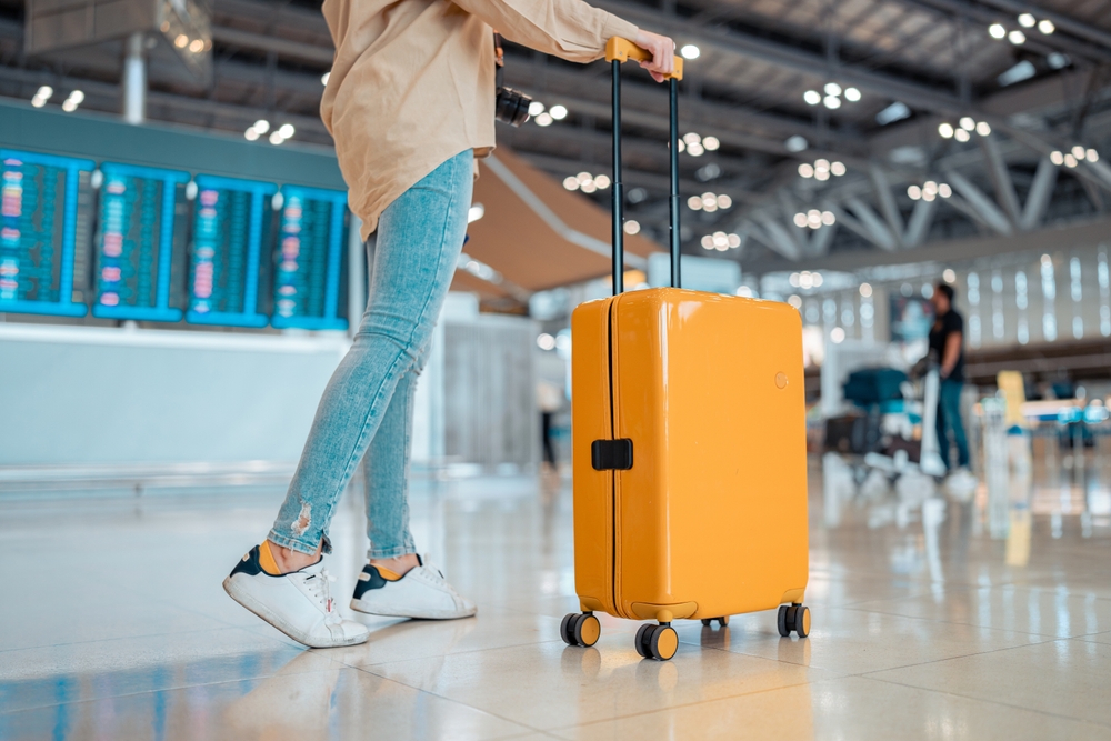 Young female traveler passenger walking with a yellow suitcase at the modern Airport Terminal